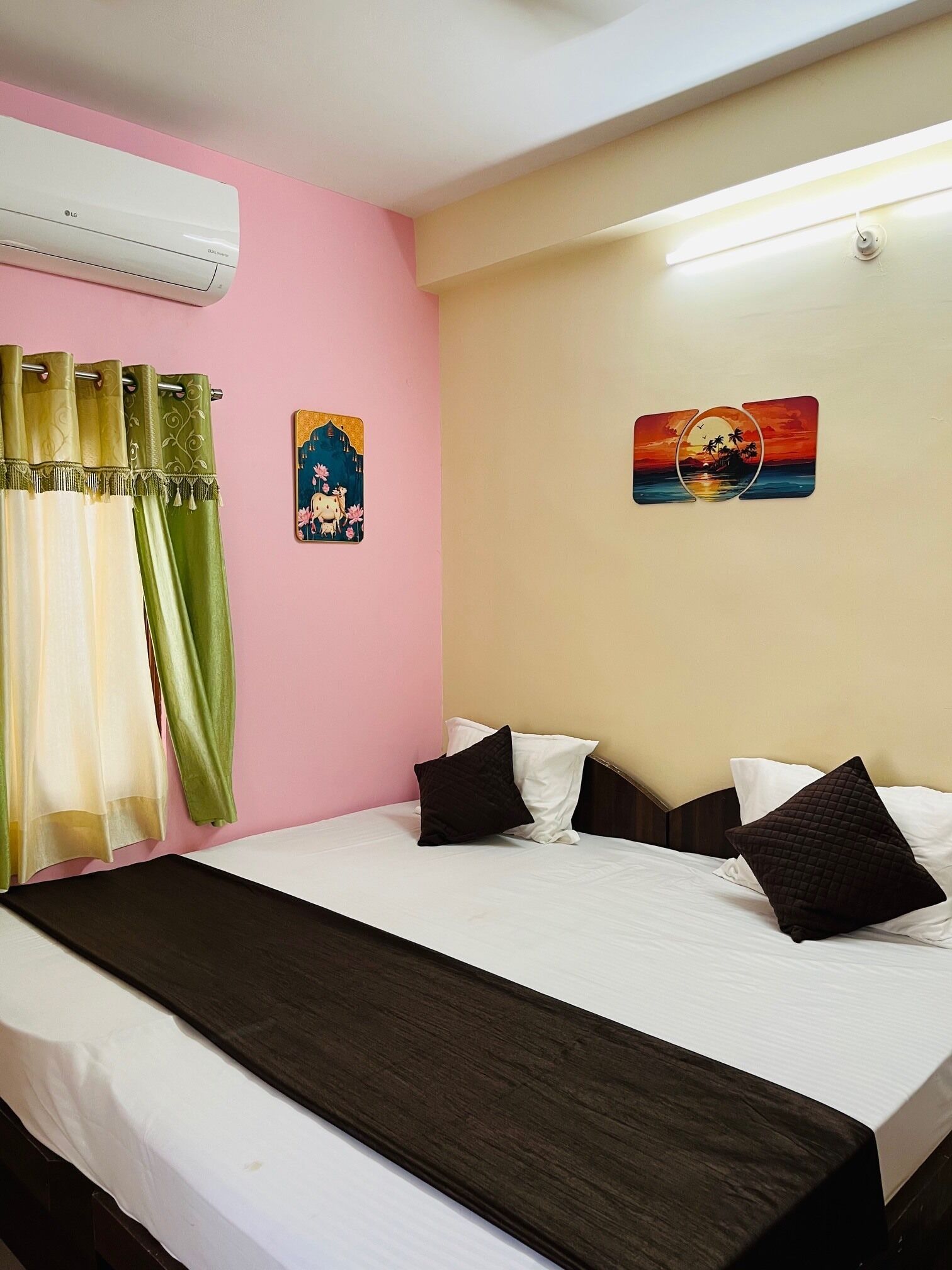 Una camera d'albergo con un letto, tende, un condizionatore d'aria a parete e due quadri appesi.