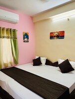 Habitación de hotel con cama, cortinas, aire acondicionado instalado en la pared y dos obras de arte en la pared.