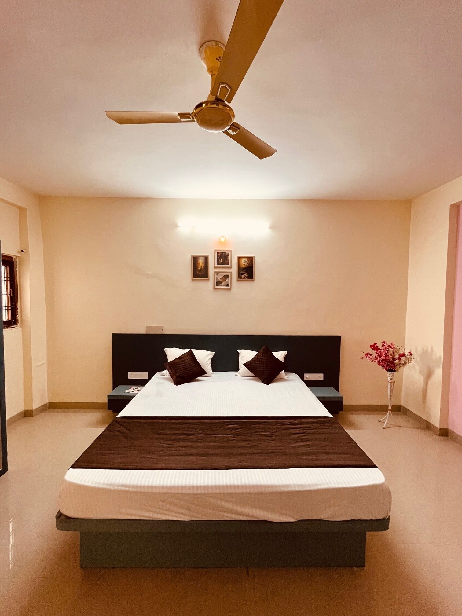A hotel room with a bed, a ceiling fan, a bedside table, and a nightstand.