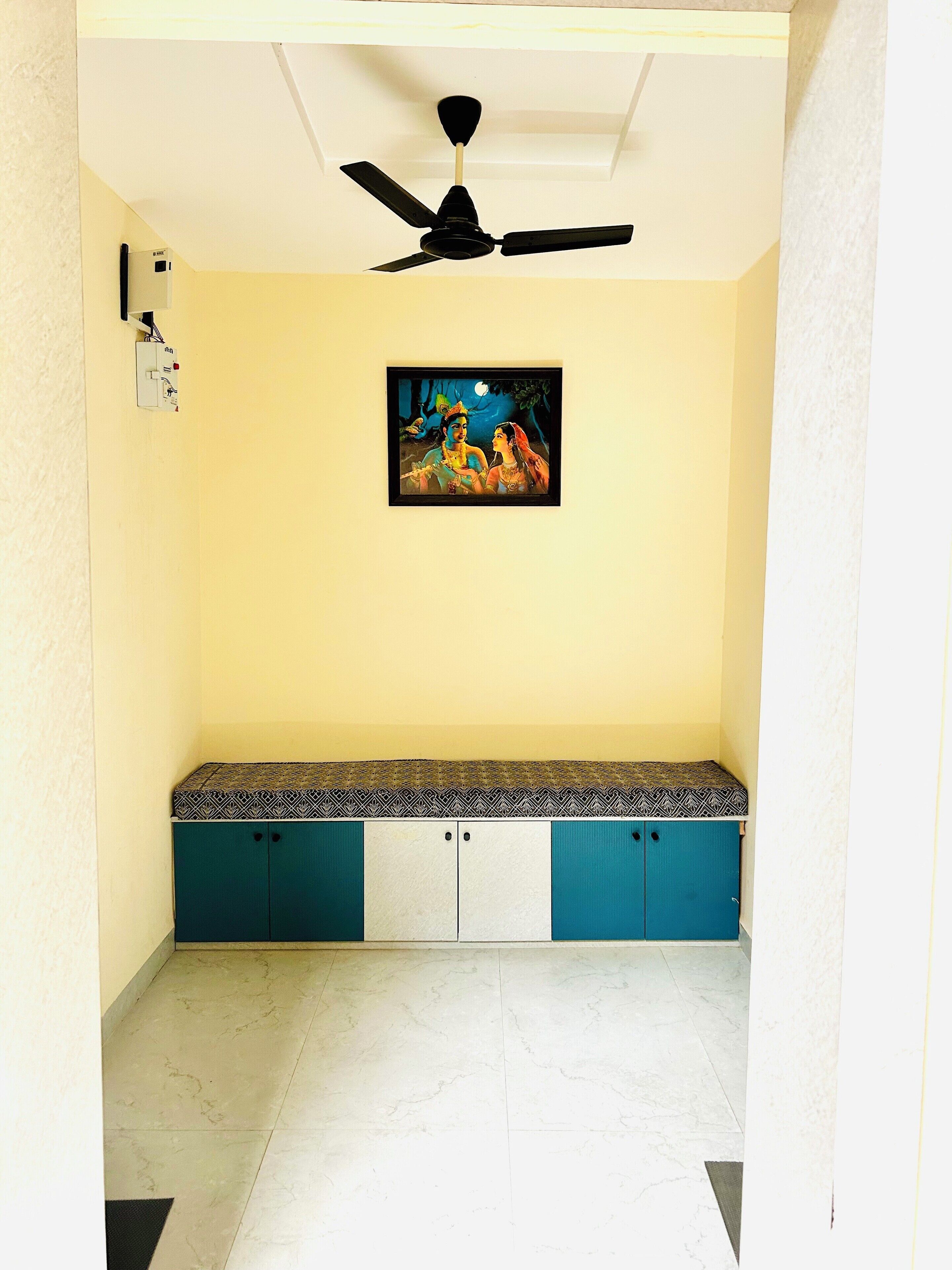 A room with a ceiling fan, a bench with patterned cushions, and a wall-mounted electrical box.