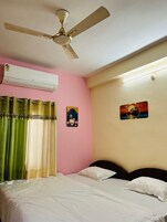 Un dormitorio con una cama, ventilador de techo, aire acondicionado, cortinas y dos adornos de pared.