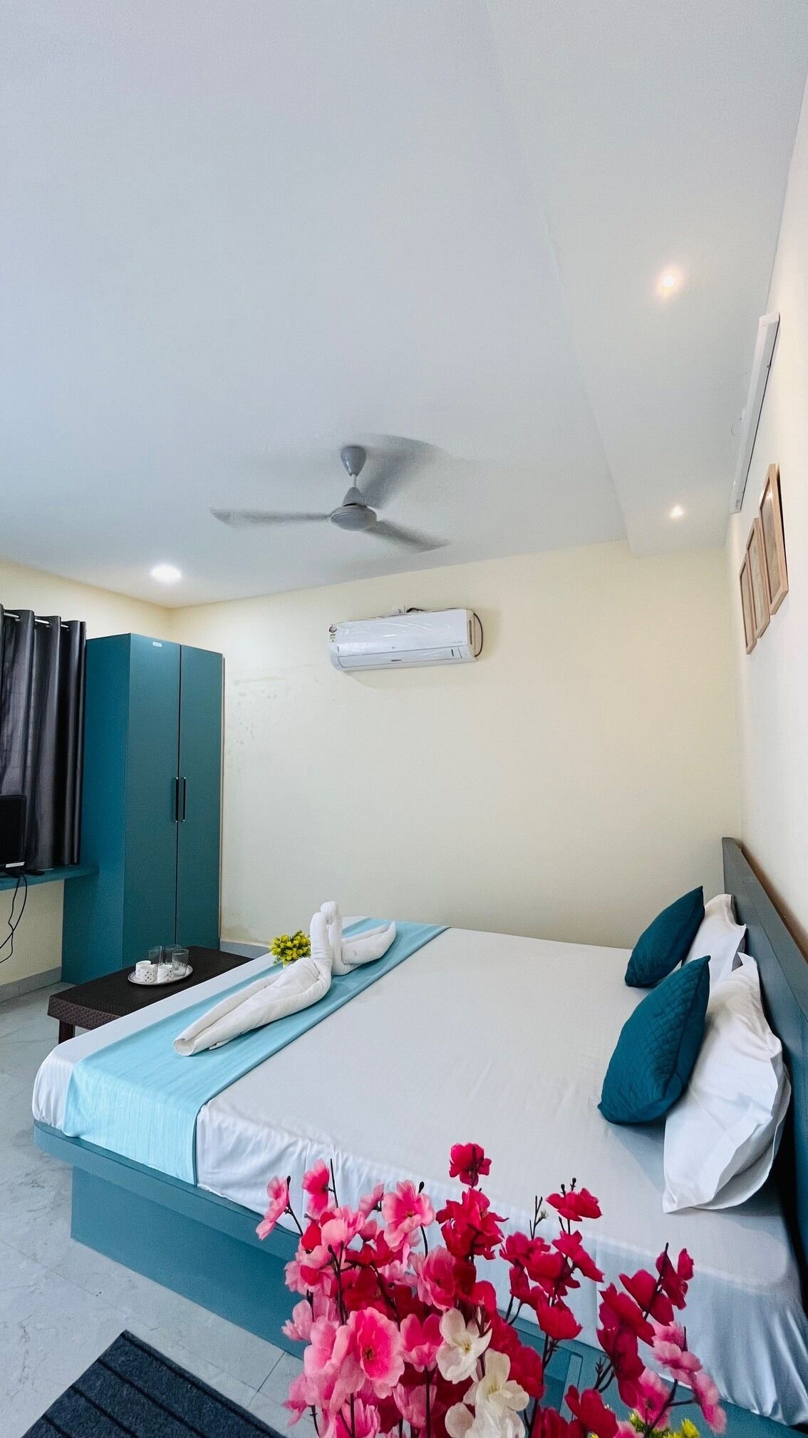 A hotel room with a bed, a ceiling fan, an air conditioning unit, a minibar, and a bathroom with a shower.