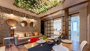 Uma sala de estar moderna com parede de pedra, teto de madeira e área de jantar com mesa posta para quatro pessoas.