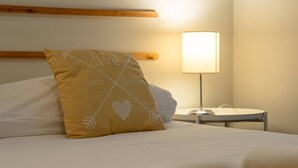 Uma cama bem arrumada, com travesseiro de design coração e flecha, luminária de cabeceira e cabeceira de madeira.