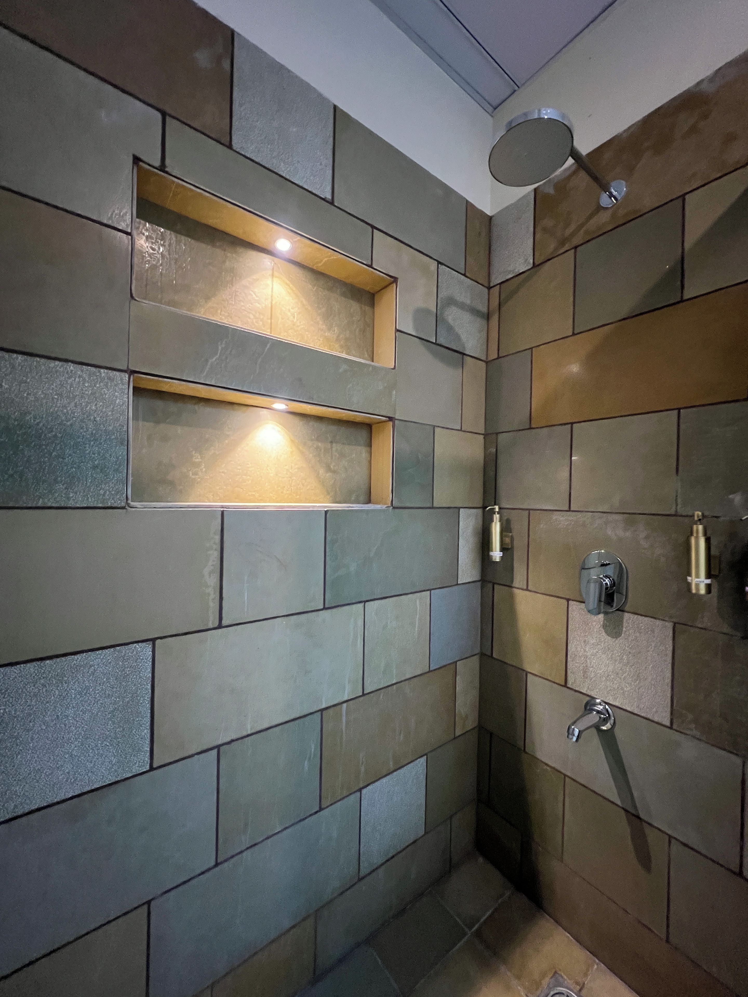 A shower area with tiled walls, a built-in shelf, and a handheld showerhead.