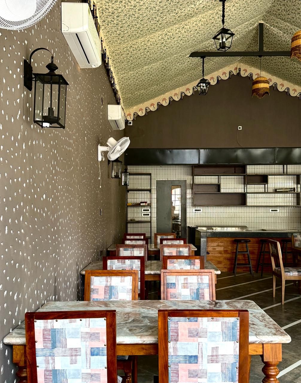 Een restaurantinterieur met tafels, stoelen, een behangwand en een keukenhoek.