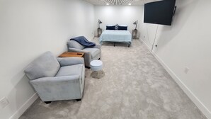 A modern, well-lit room with a grey sofa, a small ottoman, and a bed with a blue bedspread. - Adorable 3-bedroom 2-bath House in quiet, safe, kid/pet friendly neighborhood. (Enfield)