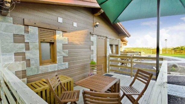A wooden deck with a table and chairs, a stone wall, and a green umbrella. - Pto calderon home beach garden (Ubiarco)