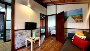 A room with a wooden ceiling, a TV mounted on the wall, a small table with a remote, a sofa with cushions, and a painting of a beach scene. - Pto calderon home beach garden (Ubiarco)