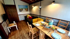 Uma área de refeições acolhedora, com mobiliário de madeira, uma mesa posta para dois e um quadro na parede.