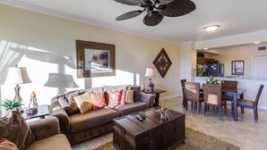 A living room with a brown sofa, a wooden coffee table, and a ceiling fan. There is a dining area with a table and chairs. - Welcome to Carefree in Calysle in Bonital Springs1 (Bonita Springs)