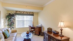 A living room with a sofa, a glass coffee table, a desk with a computer, a lamp, and a large window with blinds. - Welcome to Carefree in Calysle in Bonital Springs1 (Bonita Springs)
