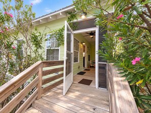 A wooden deck leading to a house with a green exterior, a door, and a ceiling fan. - Whispering Pines Cottage–Peaceful Fort Morgan Retreat | Pool | Close to Beach (Gulf Shores)