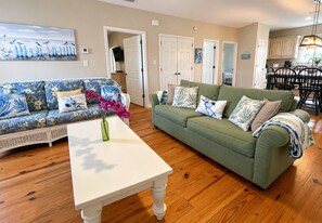 A living room with a sofa, a coffee table, and a dining area with chairs. - Whispering Pines Cottage–Peaceful Fort Morgan Retreat | Pool | Close to Beach (Gulf Shores)
