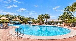Ein Swimmingpool mit Liegestühlen und Sonnenschirmen, umgeben von Bäumen und blauem Himmel.