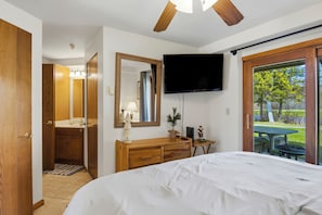 A bedroom with a bed, wooden dresser, TV, and a view of a patio with a table and chairs. - Greens & Glides Getaway at Schuss Mountain (Mancelona)