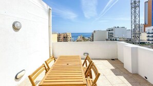 A rooftop terrace with a wooden table and chairs, a white wall, and a view of the sea and buildings. - The Joker s Penthouse at Roulette in St Julian s (St. Julian's)