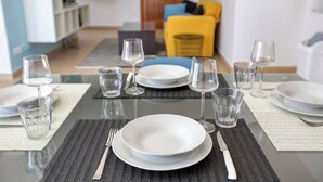A dining table set with plates, glasses, and cutlery, with a sofa and a wooden cabinet in the background. - The Joker s Penthouse at Roulette in St Julian s (St. Julian's)