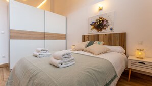 Ein modernes Schlafzimmer mit einem großen Bett, einem Holzkopfteil, einem Nachttisch mit Lampe und einem an der Wand hängenden Kunstwerk.