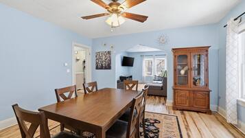 A dining room with a wooden table and chairs, a ceiling fan, and a patterned rug.