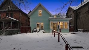 Une maison à deux étages, avec une façade verte, un porche à l’avant et une porte d’entrée bien visible.