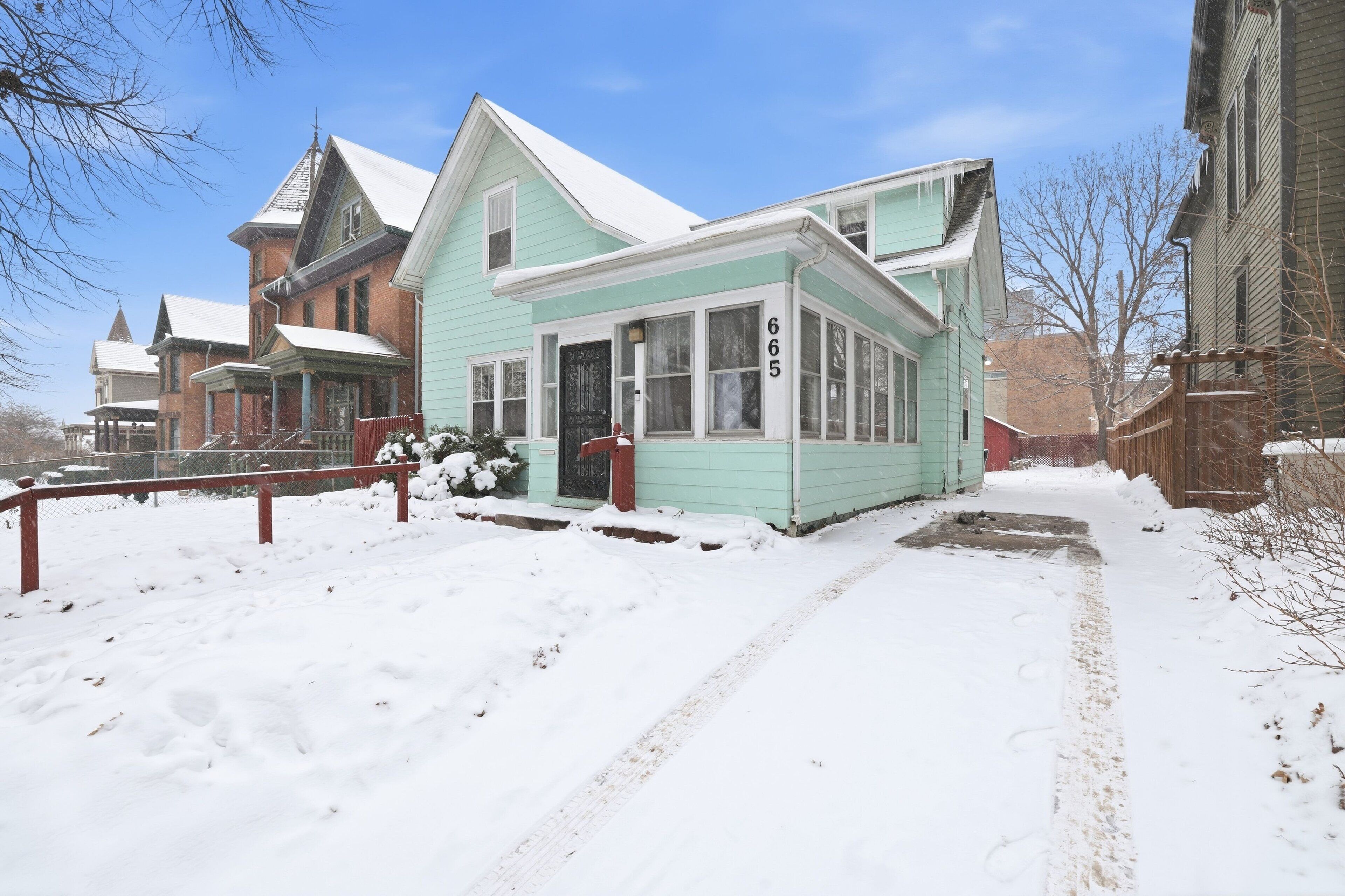A historic building with a prominent number '665' on the front, surrounded by snow-covered ground and a wooden fence.