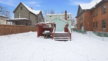 A snow-covered backyard with a wooden fence, a small shed, and a brick building.