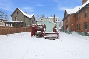 Een sneeuwbedekte achtertuin met een houten hek, een kleine schuur en een gebouw van baksteen.
