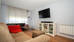Un salon avec un canapé beige, un coussin rouge, un meuble blanc aux portes vitrées et un téléviseur à écran plat fixé au mur.