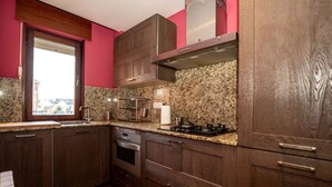Une cuisine avec des meubles de couleur bois foncé, des comptoirs en granit, une hotte de cuisinière en acier inoxydable et une fenêtre équipée de stores.
