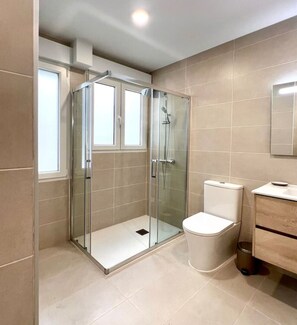 Une salle de bain moderne avec une douche à parois de verre, des toilettes et un meuble-lavabo avec un miroir.