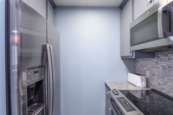A compact kitchen with a stainless steel refrigerator, a microwave, a toaster, and a built-in oven. - Bridges 76 2 Bedroom Condo (Warren)