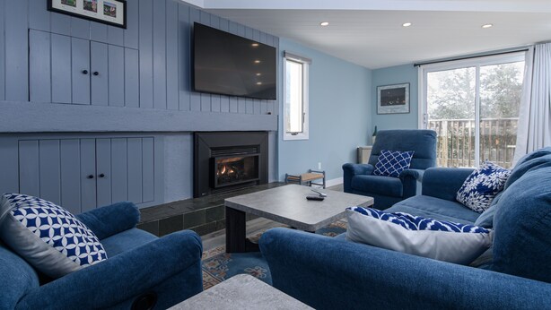 Una sala de estar moderna con muebles azules, una chimenea y un ventanal grande.