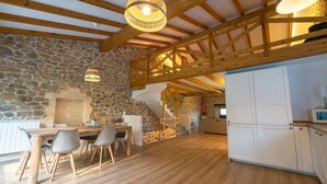 A rustic interior with exposed wooden beams, stone walls, a wooden dining table with chairs, and a kitchen area with cabinets. - The Stone House – naturaleza y confort (villacarriedo)