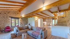 A spacious living room with a stone wall, a wooden ceiling, and a cozy sofa. - The Stone House – naturaleza y confort (villacarriedo)