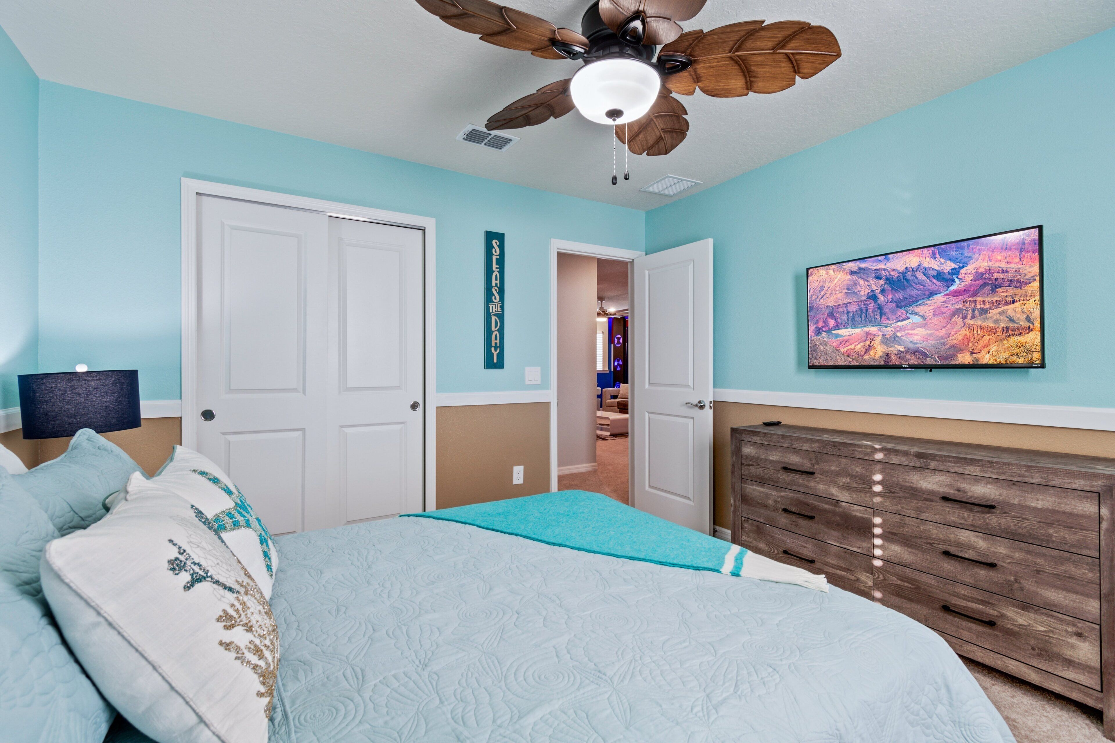 A bedroom with a bed, a ceiling fan, a dresser, and a wall-mounted TV.