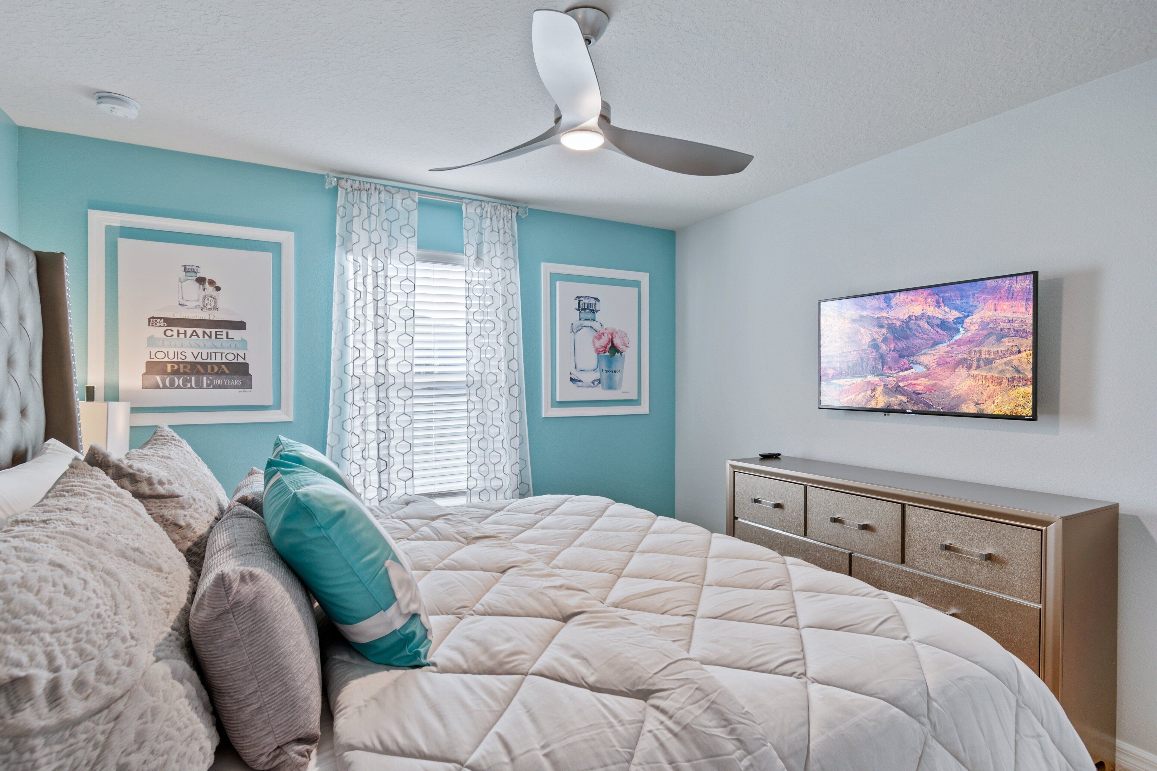 Una camera da letto con un letto, una ventola a soffitto, una TV e quadri appesi al muro.