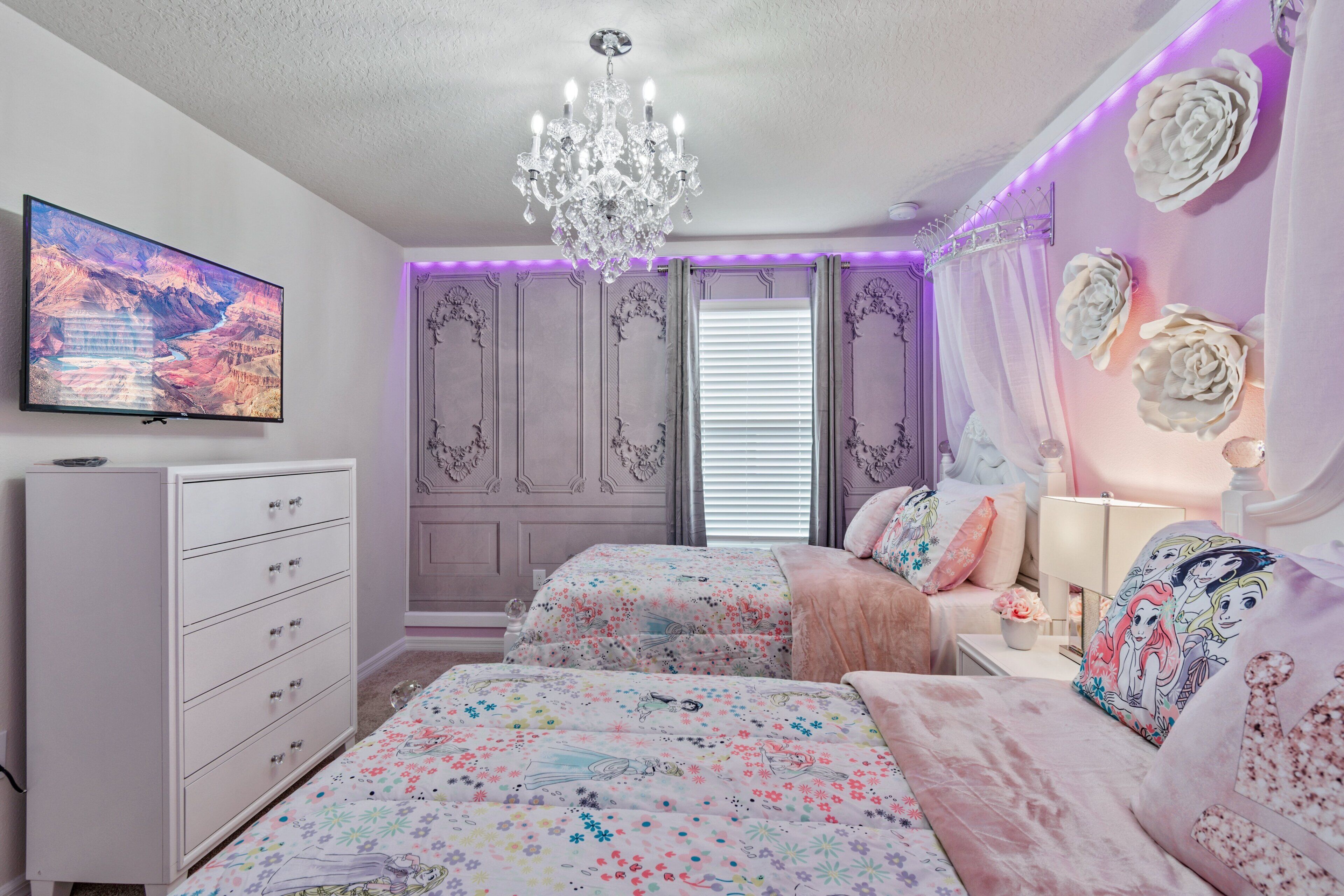 A bedroom with a TV, chandelier, floral bedding, and decorative pillows.