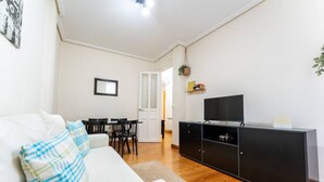 A living room with a white sofa, a black entertainment unit, and a dining area with a table and chairs. - Your Bright Retreat in the Heart of Santander (Santander)