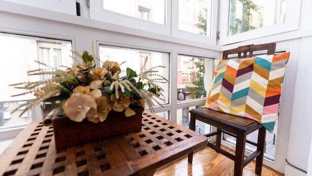 A wooden table with a floral arrangement and a colorful chevron-patterned pillow on a chair. - Your Bright Retreat in the Heart of Santander (Santander)