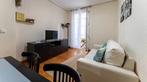 A living room with a sofa, a TV on a cabinet, a dining table with chairs, and a sliding glass door leading to a balcony. - Your Bright Retreat in the Heart of Santander (Santander)