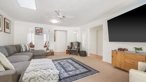 Ein Wohnzimmer mit grauem Sofa, einem gemusterten Teppich, einem Holzkabinett und einem großen Fernseher.