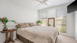 Ein Schlafzimmer mit einem Bett, zwei Nachttischen, einem Deckenventilator und zwei Fenstern mit Jalousien.