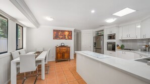 Eine moderne Küche mit weißen Schränken, ein Essbereich mit weißem Tisch und Stühlen sowie ein großes Fenster für natürliches Licht.
