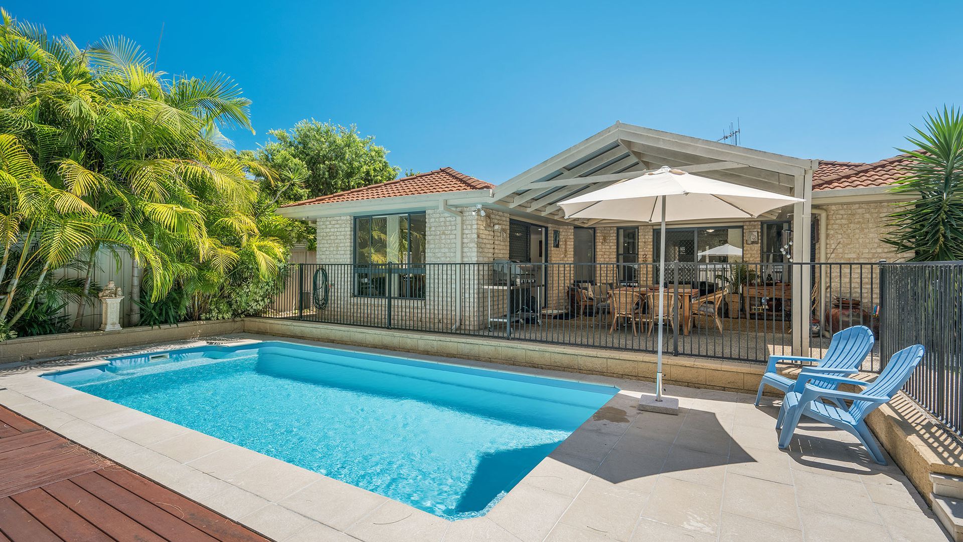 Una piscina con zona de patio, mobiliario exterior y un área de estar cubierta.