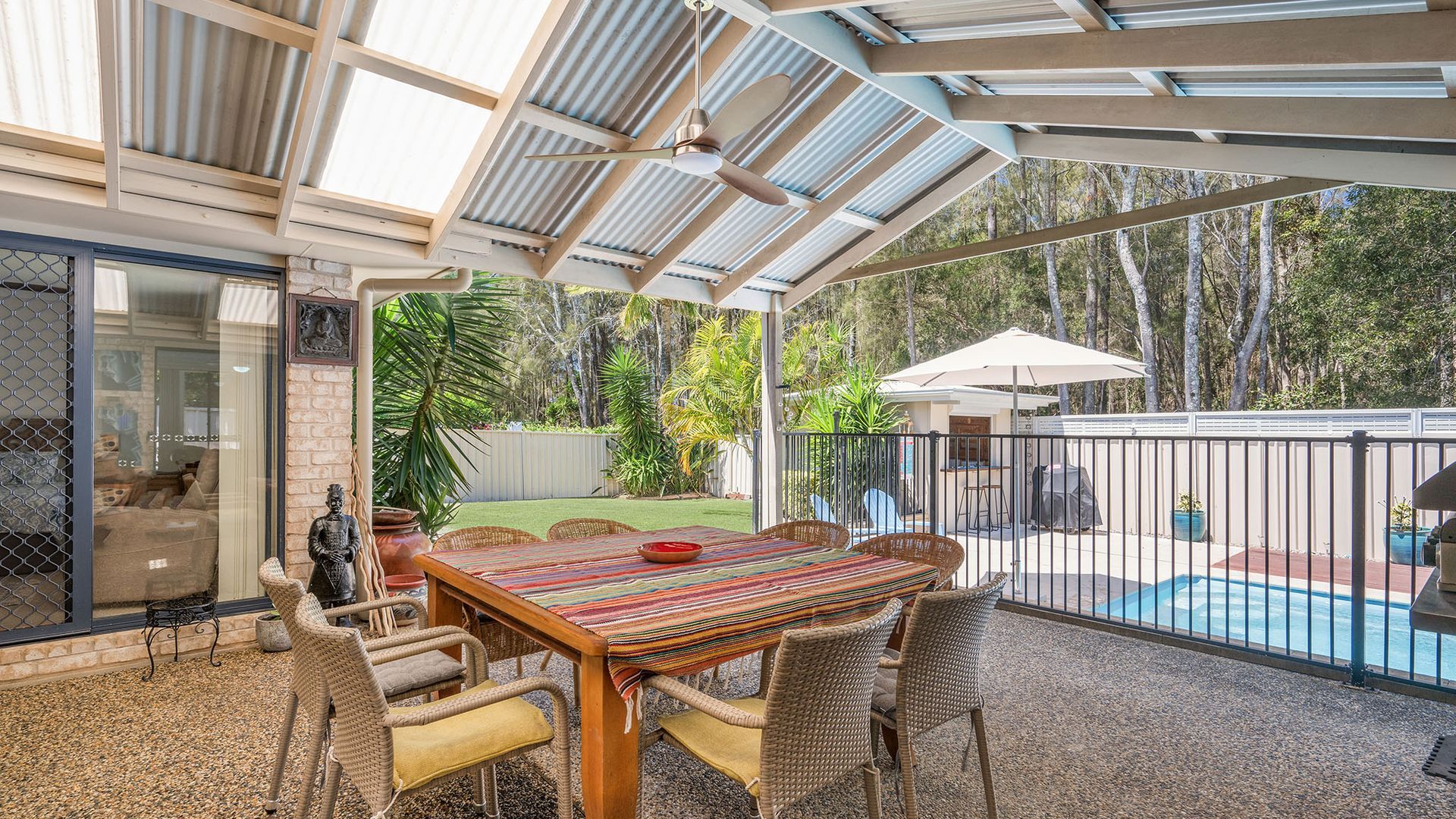 Un patio cubierto con piscina, mobiliario exterior y vista al jardín trasero.