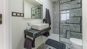 Ein modernes Badezimmer mit einem weißen Waschbecken, einem Spiegel, einer Duschkabine und einer Rückwand aus Granit.