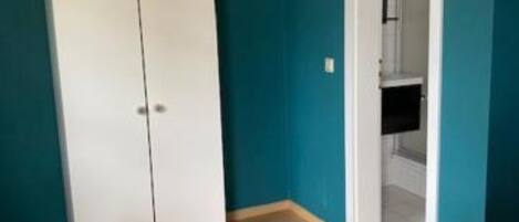 A room with teal walls, a white wardrobe, and a wooden floor.