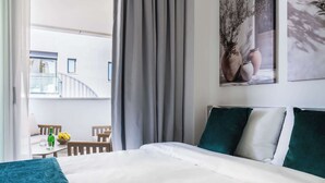 A hotel room with a bed, a view of the outside balcony, and a painting on the wall. - Modern Studio Suite w/ Balcony & Queen Bed – Germasogeia Tourist Area, Limassol (Germasogeia)