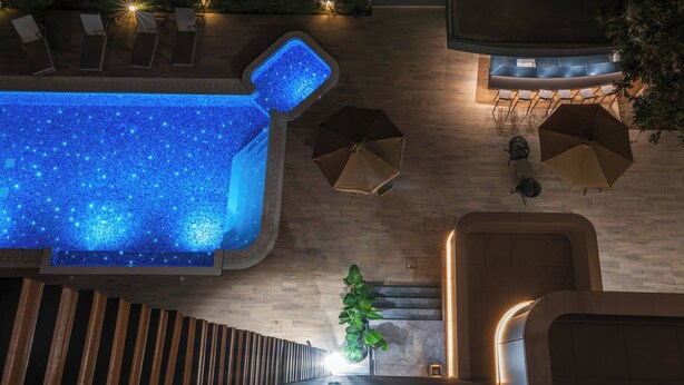 A rooftop pool area with a blue-lit pool, lounge chairs, and umbrellas. - Modern Studio Suite w/ Balcony & Queen Bed – Germasogeia Tourist Area, Limassol (Germasogeia)
